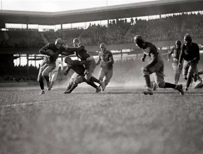 Princeton and Dartmouth players colliding mid-play in a packed 1951 stadium, black and white.